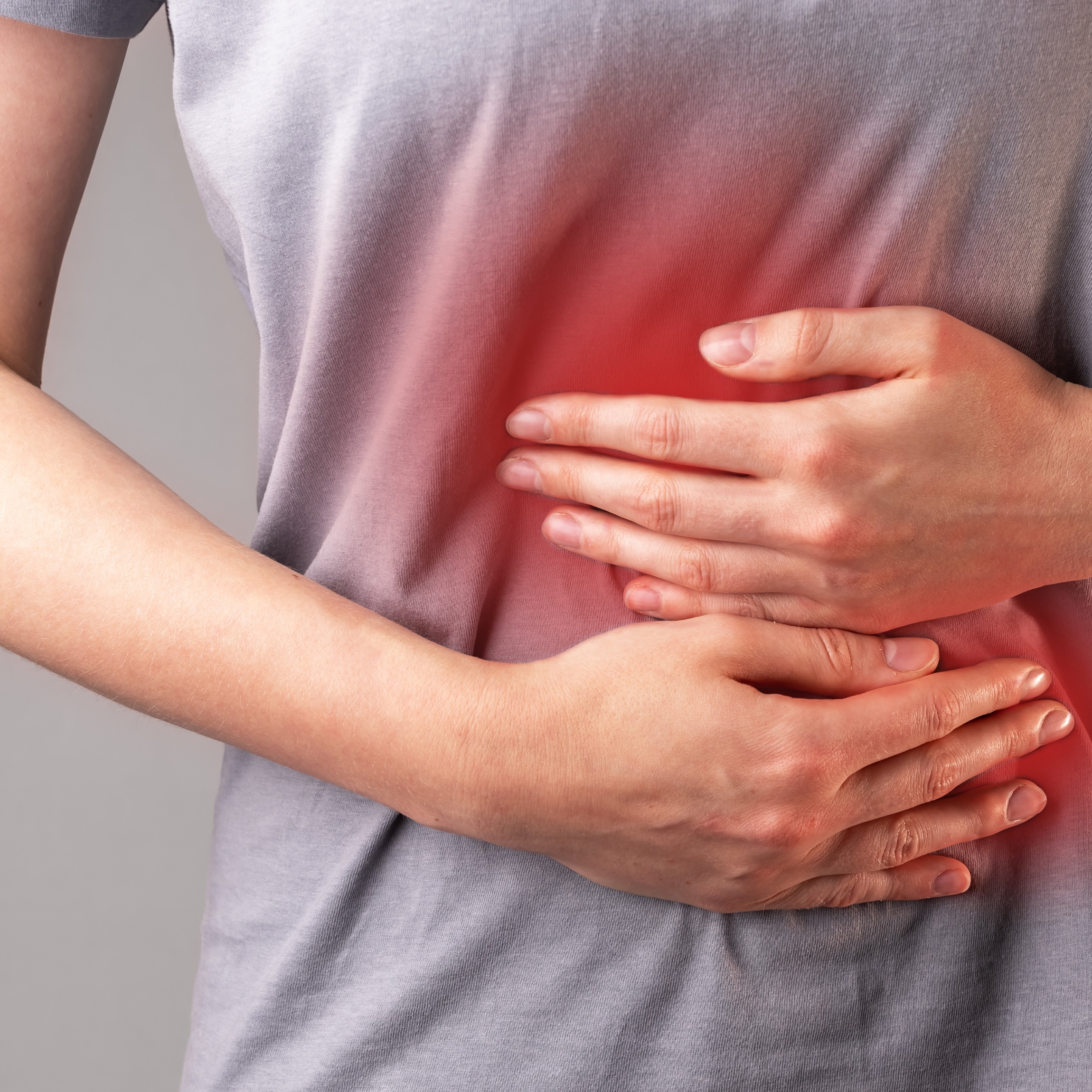 What Makes Celiac Disease Ayurveda Treatment Different from Conventional Care A person clutching their abdomen with both hands, indicating stomach pain or discomfort. The red gradient overlay on the stomach area visually represents internal pain or inflammation, possibly related to digestive issues or gastrointestinal distress.