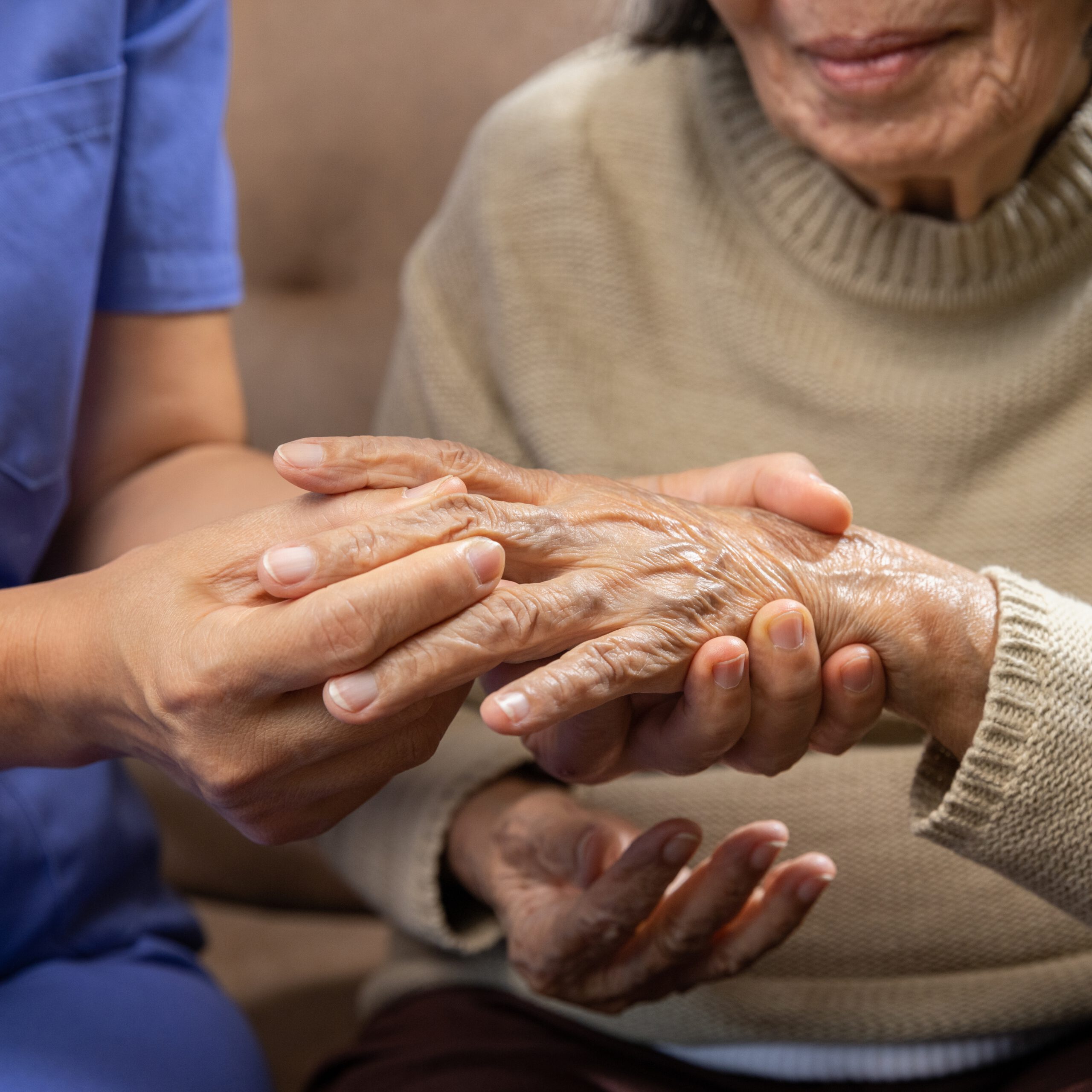 A close-up of a caregiver gently holding the hand of an elderly woman, whose fingers show signs of joint stiffness or deformity, symbolizing care and support for someone living with rheumatoid arthritis.