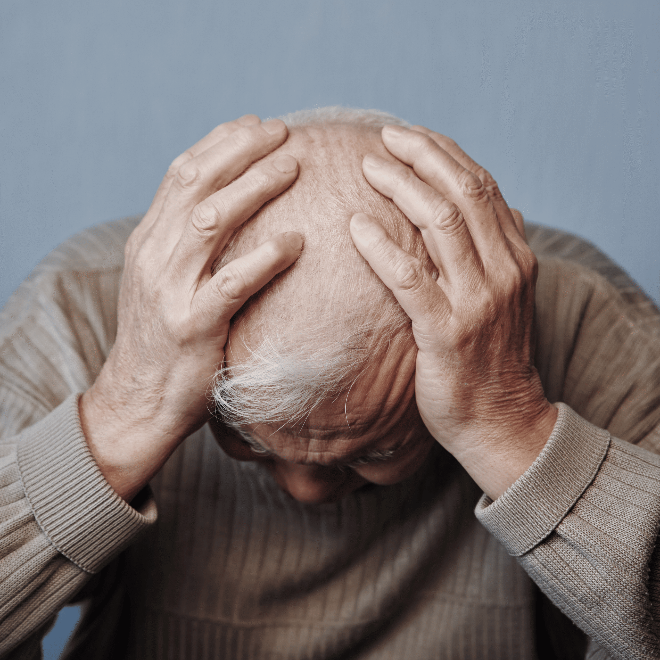 Elderly man holding his head in distress, symbolizing pain and neurological challenges related to multiple sclerosis.