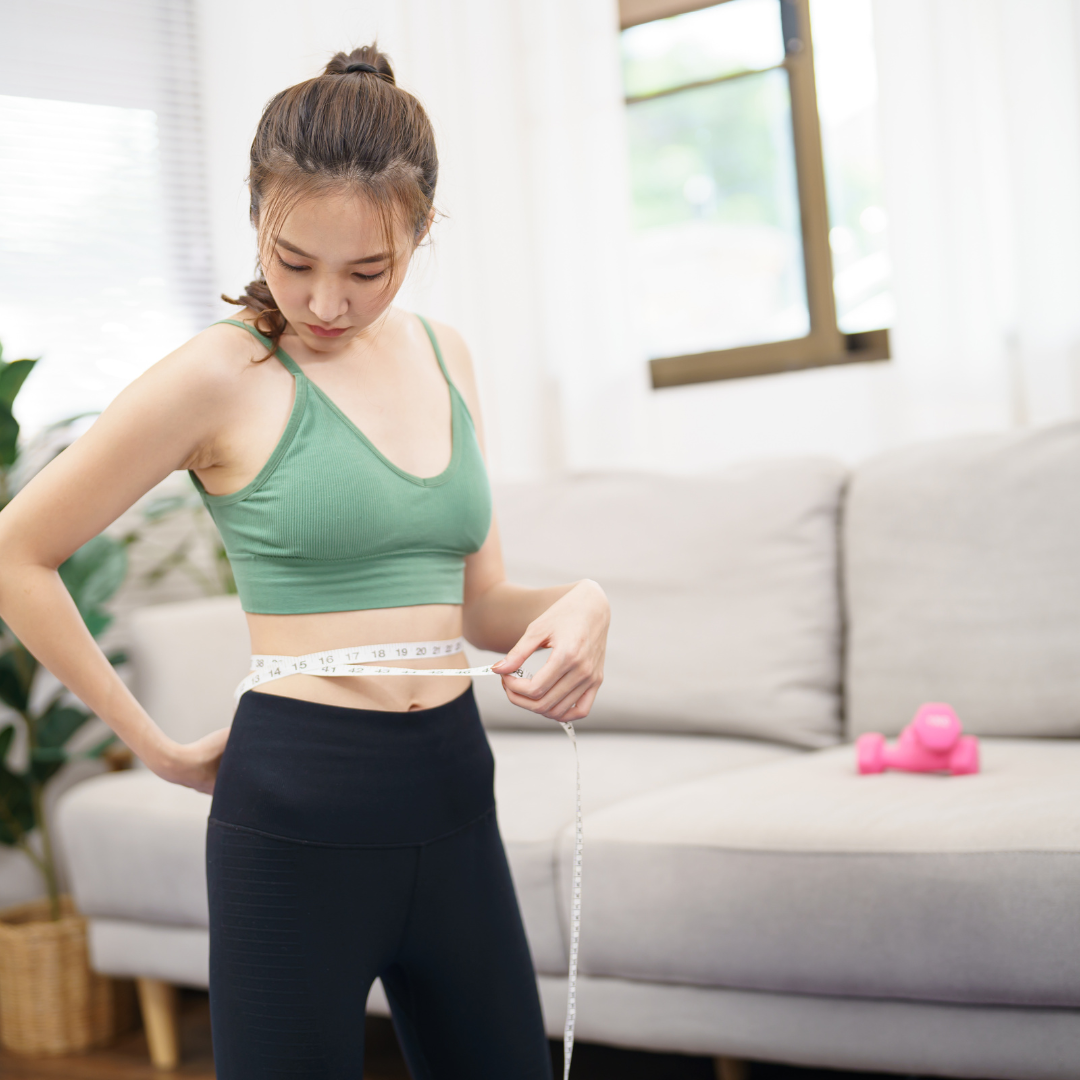 Young woman measuring her waistline after workout, symbolizing natural weight management at the best Ayurvedic weight loss centre in Kerala.
