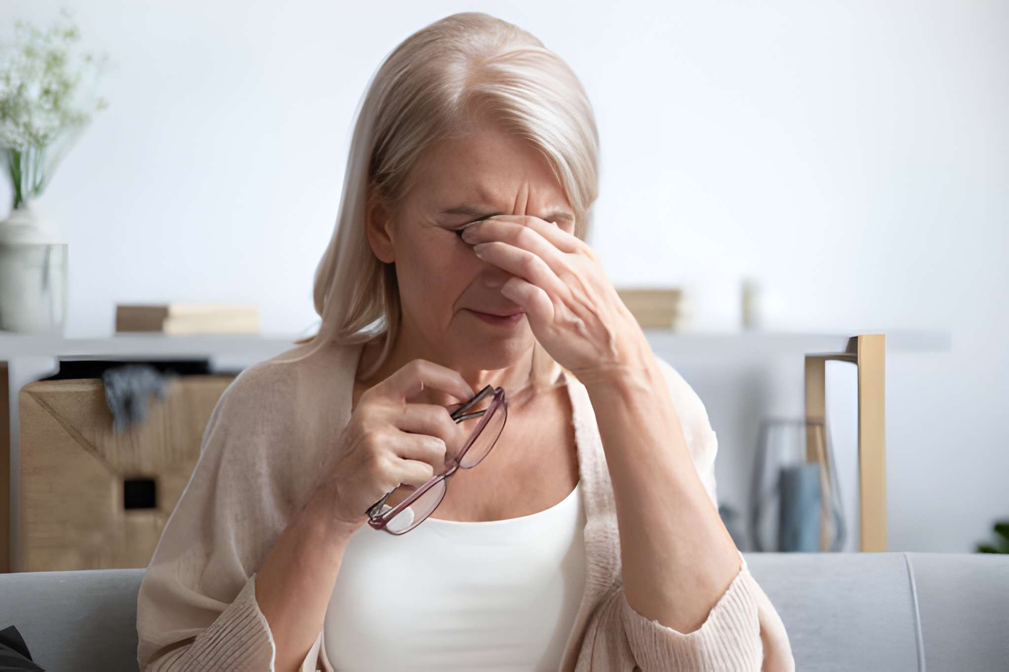 Woman rubbing her tired dry eyes while holding glasses, showing discomfort; representing natural ways to treat dry eyes through Ayurvedic and holistic care.